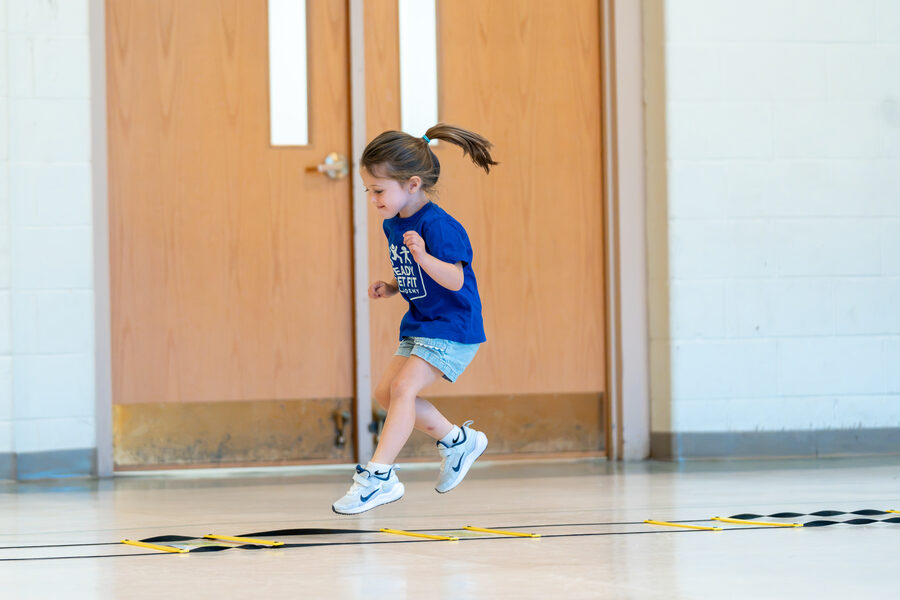 Preschooler mid-air over an agility ladder during a Ready Set Fit class